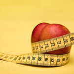 Crash-Diät / Roter Apfel mit Maßband auf gelbem Hintergrund – Symbol für Diäten, Ernährung und Gewichtsverlust