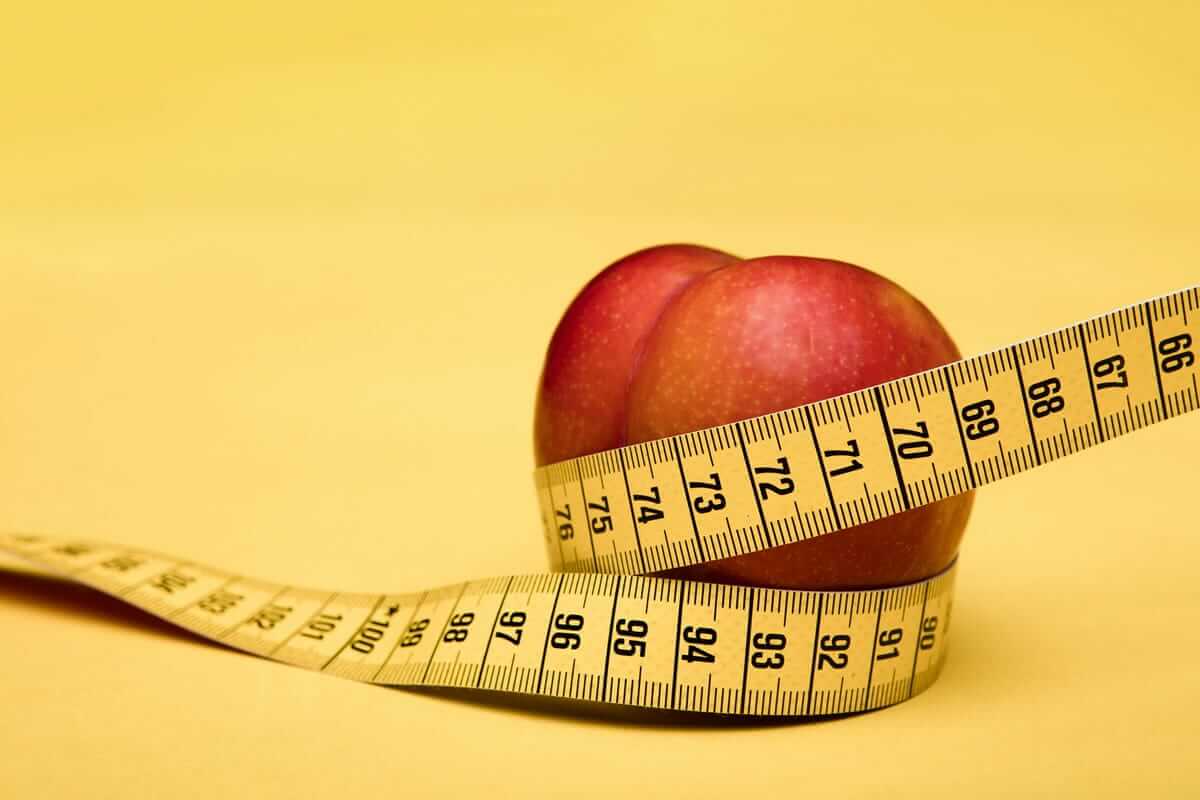 Crash-Diät / Roter Apfel mit Maßband auf gelbem Hintergrund – Symbol für Diäten, Ernährung und Gewichtsverlust
