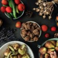 Verschiedene ballaststoffreiche Lebensmittel von oben – Walnüsse, Feigen, Tomaten, Äpfel, Gurken und Gemüse auf dunklem Untergrund