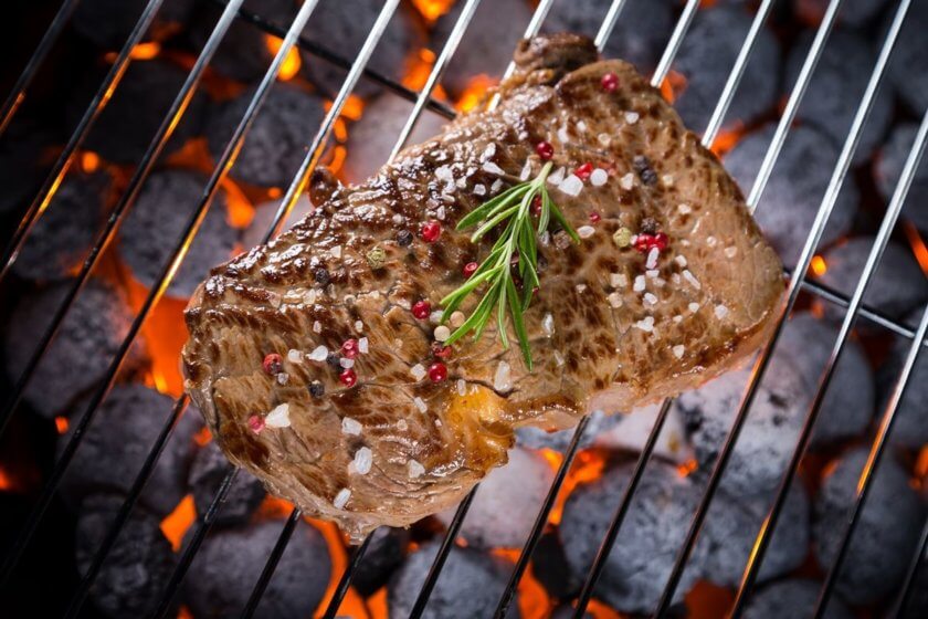 Grillen & Sous-Vide-Garen (Saftiges Steak mit grobem Salz, Pfeffer und Rosmarin auf dem Grillrost über glühenden Kohlen)
