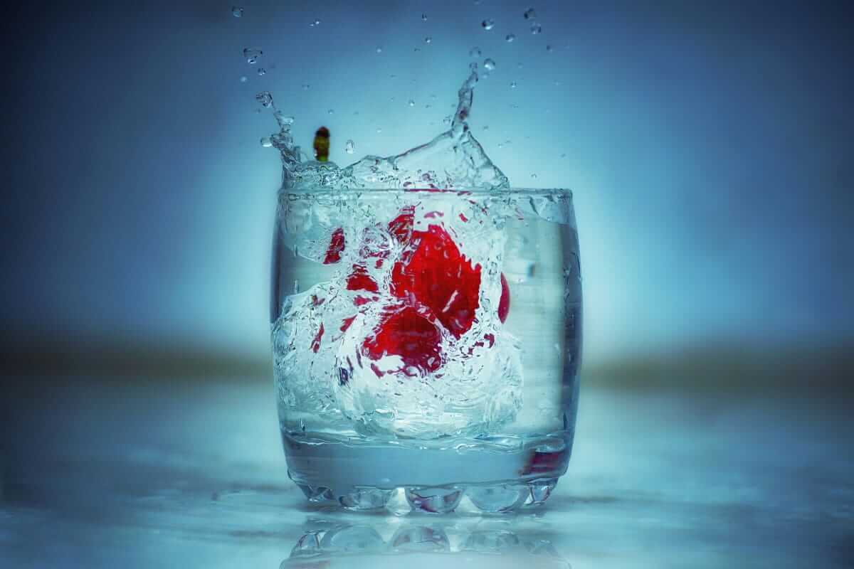 Kirsche fällt in ein Glas Wasser – ausreichend trinken hilft bei Gicht, Harnsäure auszuscheiden