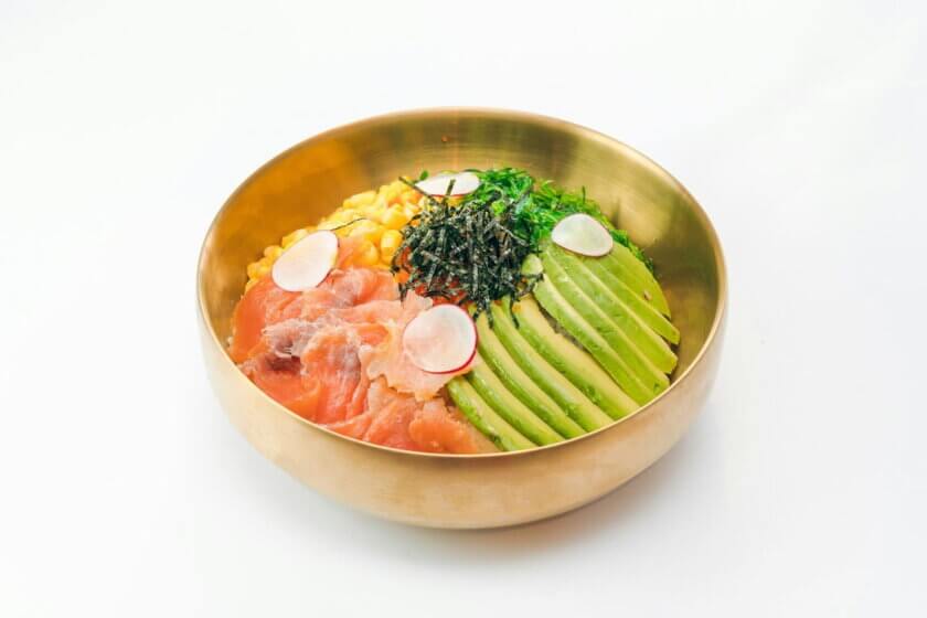 flexitarisch genießen / Bunte Bowl mit Avocado, Lachs, Mais, Algen und Radieschen in goldener Schale – Symbol für flexitarische Ernährung mit bewusster Auswahl.