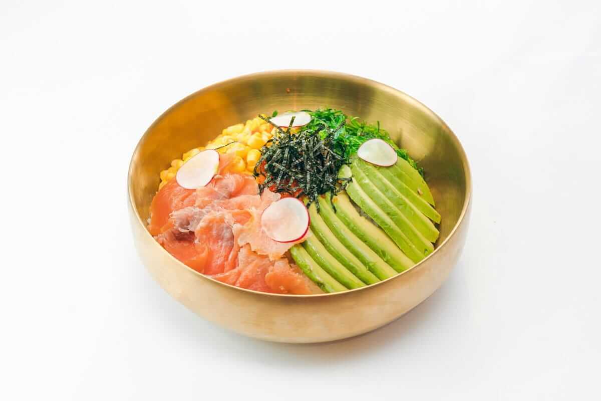 flexitarisch genießen / Bunte Bowl mit Avocado, Lachs, Mais, Algen und Radieschen in goldener Schale – Symbol für flexitarische Ernährung mit bewusster Auswahl.