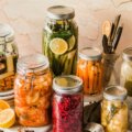 Fermentieren (Verschiedene Einmachgläser mit fermentiertem Gemüse wie Karotten, Rote Bete, Kimchi und Gurken – dekorativ arrangiert auf einem hellen Untergrund)