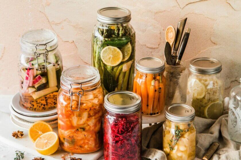 Fermentieren (Verschiedene Einmachgläser mit fermentiertem Gemüse wie Karotten, Rote Bete, Kimchi und Gurken – dekorativ arrangiert auf einem hellen Untergrund)