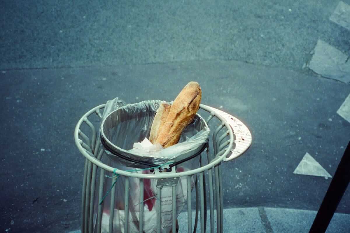Food Waste / Frisches Baguette in einem Mülleimer auf der Straße – Symbol für Lebensmittelverschwendung im Alltag