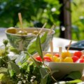 Sommer, Abnehmen (Sommerliche Snacks mit bunten Tomaten und Oliven in Schälchen auf einem hell gedeckten Tisch im Grünen – leichtes, gesundes Essen im Sonnenschein)