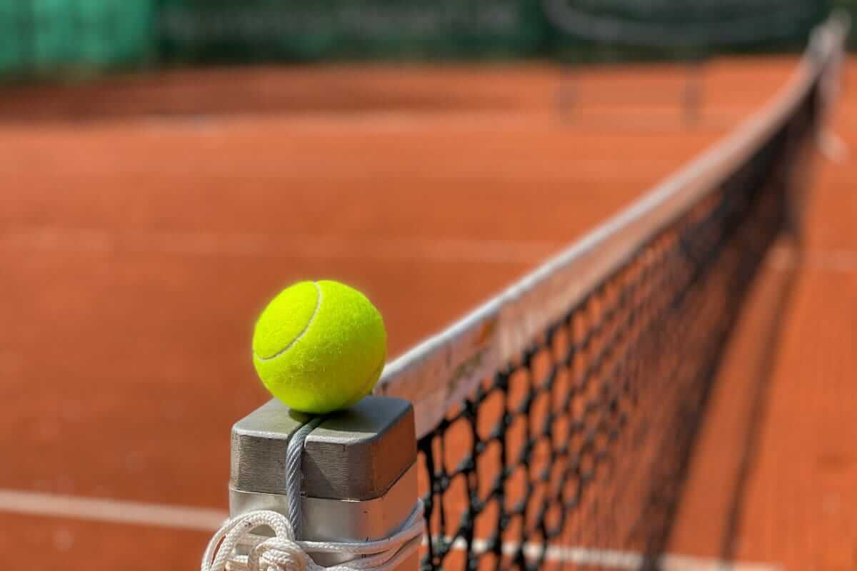 Tennis - stressfrei abnehmen (Tennisball liegt auf dem Netzpfosten eines Sandplatzes – Symbol für den Moment der Entscheidung und den Start in etwas Neues.)