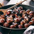 Maronen, Esskastanien (Geröstete Maronen in einer Pfanne mit Holzlöffel, frisch aufgeplatzt und dampfend, als herbstliche Spezialität serviert.)