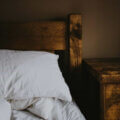 Schlaf / Holzbett mit weißem Kopfkissen und gedämpftem warmem Licht – ein ruhiger, gemütlicher Schlafplatz