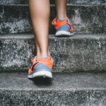 Person geht eine Steintreppe hinauf, Fokus auf den Sportschuhen – symbolisiert Bewegung im Alltag.