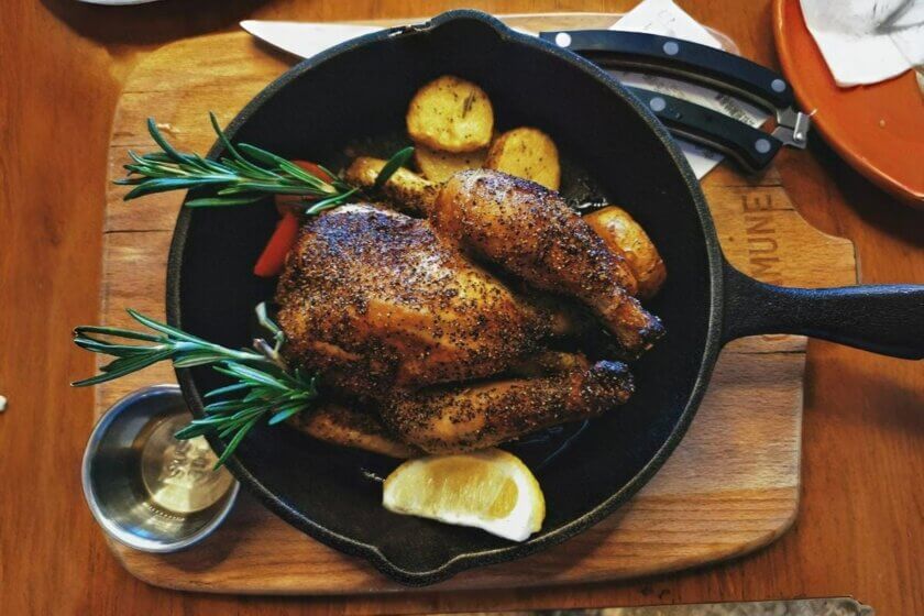 Goldbraun gebratenes Geflügel mit Rosmarin und Kartoffeln in gusseiserner Pfanne – herbstliches Festessen zum Martinstag / Martinsgans