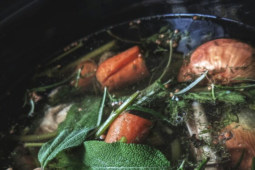 Brühe, Fonds & Soßen / Frische Gemüse- und Kräuterstücke wie Karotten, Zwiebeln und Salbeiblätter, die in einem Topf zu einer aromatischen Gemüsebrühe köcheln.