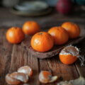Mandarinen auf einem rustikalen Holztisch, eine davon geschält, mit warmem Winterlicht.