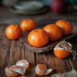 Foto: <a href="https://unsplash.com/de/fotos/ein-korb-mit-orangen-JTUL22JUi9o" target="_blank" rel="noopener">Mila / unsplash.com</a> Mandarinen auf einem rustikalen Holztisch, eine davon geschält, mit warmem Winterlicht.