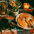 Warm gedeckter Frühstückstisch mit Pancakes, Obstschale und Kerze als gemütliches Mood-Food-Setting.