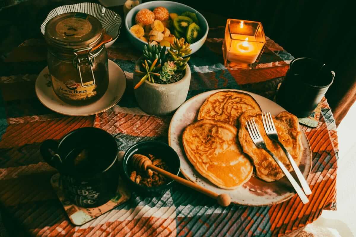 Warm gedeckter Frühstückstisch mit Pancakes, Obstschale und Kerze als gemütliches Mood-Food-Setting.
