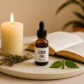 CBD-Öl-Flasche mit Pipette auf Tablett neben Kerze, Buch und getrockneten Kräutern – Symbol für Entspannung, Achtsamkeit und einen gesunden Lebensstil.