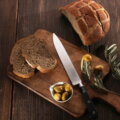 Schlichtes Arrangement aus Brot, Oliven und einem Messer auf einem Holzbrett als Symbol für einfache, wenig verarbeitete Lebensmittel