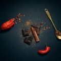 Dunkle Schokolade, rote Chilischoten, Zimtstangen und Chilipulver auf dunklem Untergrund – Zutaten für Swicy Food