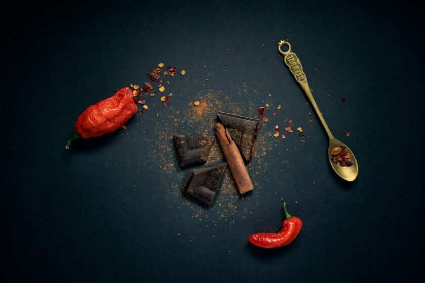 Dunkle Schokolade, rote Chilischoten, Zimtstangen und Chilipulver auf dunklem Untergrund – Zutaten für Swicy Food