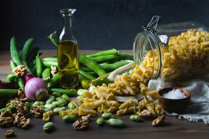 Ausgewogene Ernährung: Frische Zutaten wie Gemüse, Pasta, Olivenöl und Hülsenfrüchte auf rustikaler Arbeitsfläche – Symbol für Vielfalt und Balance im Alltag