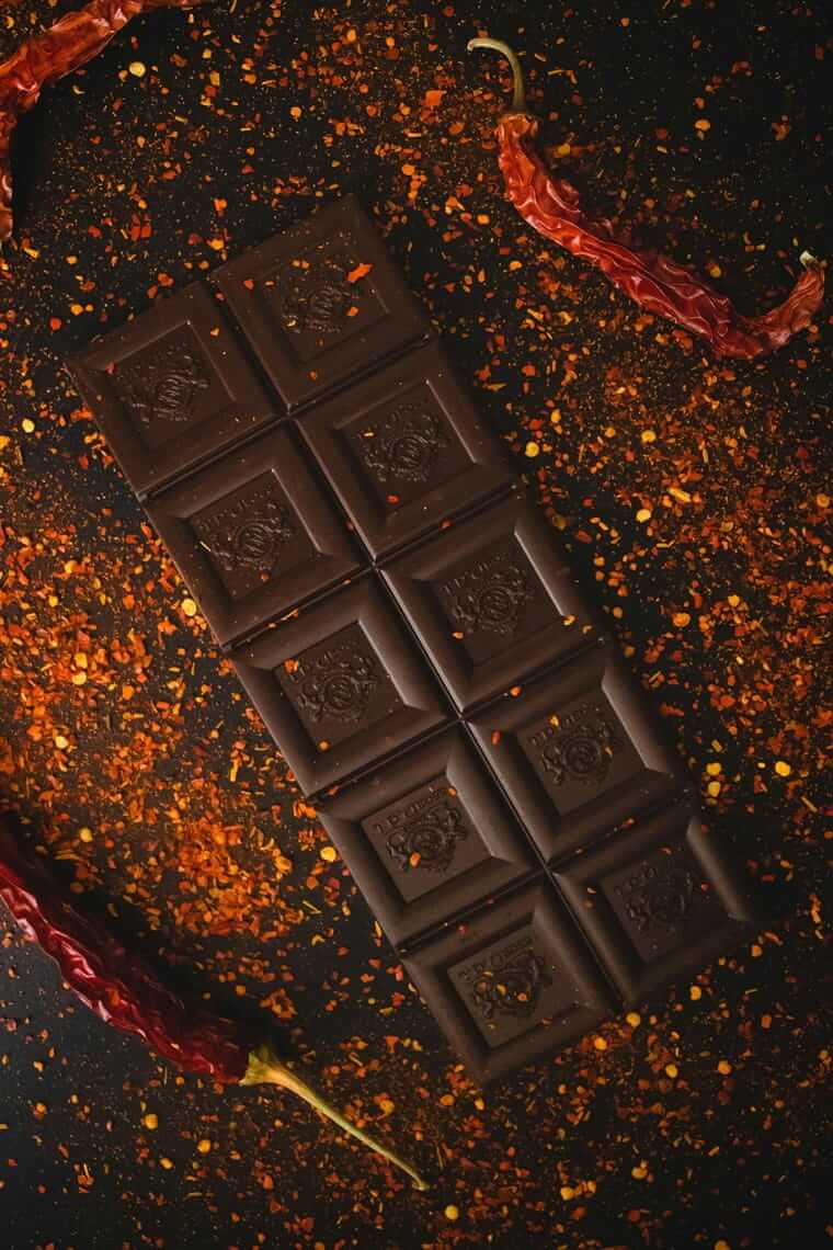 Swicy Food: Wenn süß auf scharf trifft – und warum das nicht verrückt ist Detailansicht: Getrocknete Chilischote auf dunkler Schokolade mit leuchtenden Chiliflocken