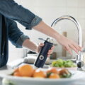 Leitungswasser / Person füllt wiederverwendbare Trinkflasche mit Leitungswasser am Küchenhahn – nachhaltige Alternative zu Mineralwasser