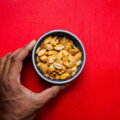 Snacken / Hand hält eine Schüssel mit gerösteten Kürbiskernen vor rotem Hintergrund