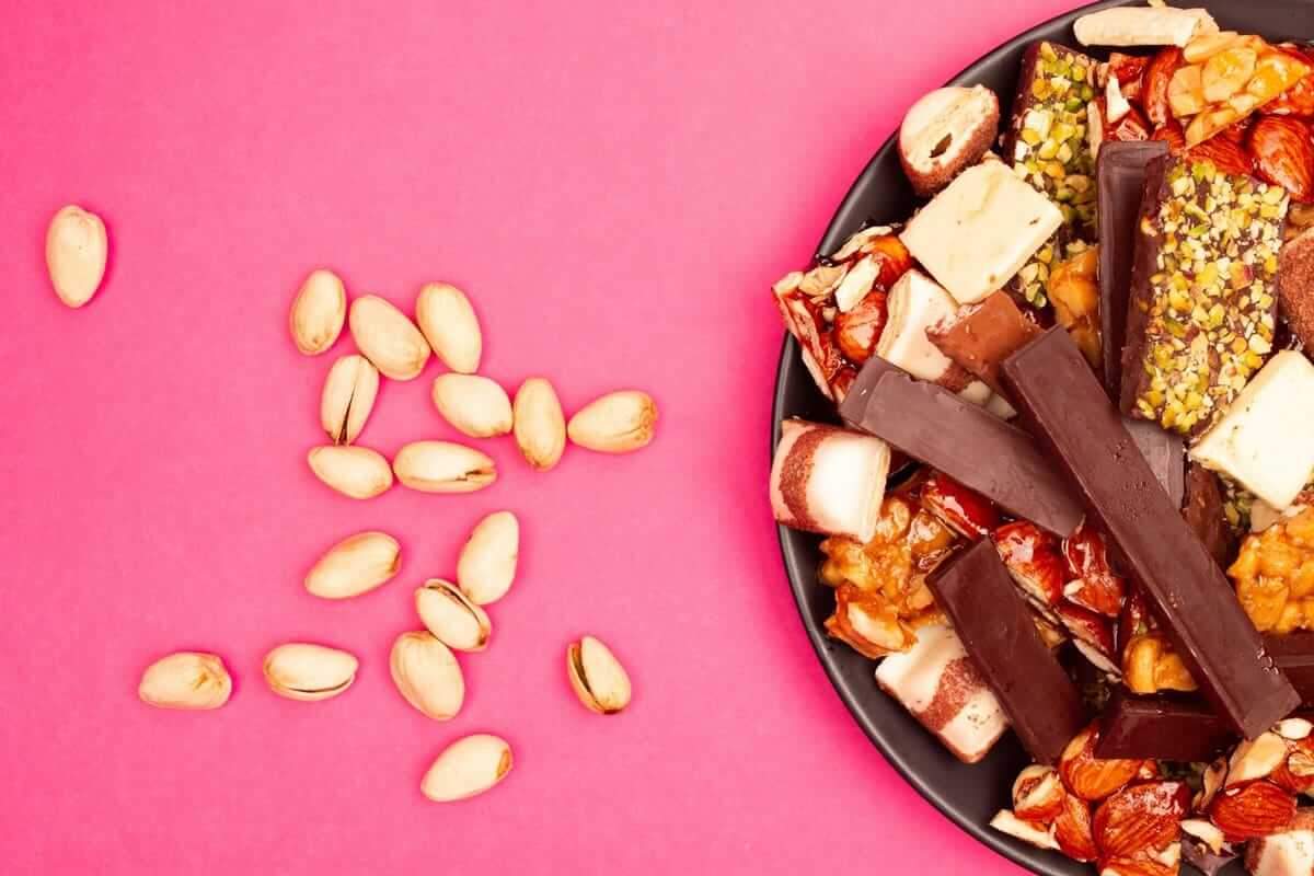 Snacken / Teller mit Schokoladenstücken, Nüssen und Süßigkeiten auf pinkfarbenem Untergrund