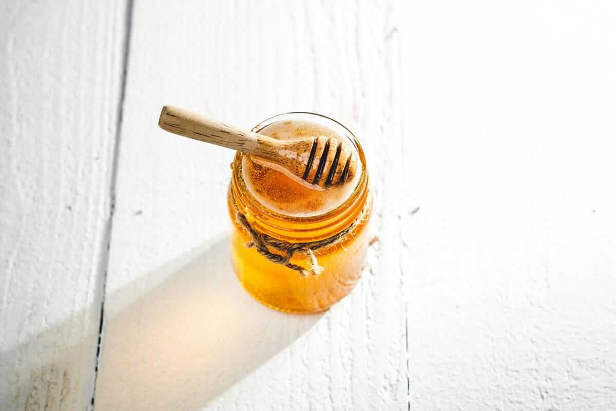 Manuka Honig / Honigglas mit Holzlöffel auf weißem Holzuntergrund