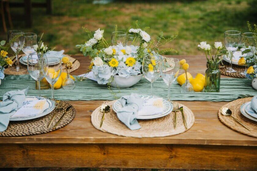 Gedeckter Gartentisch mit Zitronen, Blumendeko und Stoffservietten für eine Catering-Feier im Freien