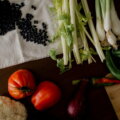 einfache Gerichte / Schwarze Bohnen, Tomaten, Blumenkohl und Frühlingszwiebeln auf einem Holzbrett – unverarbeitete Grundzutaten als Basis klimafreundlicher Ernährung.