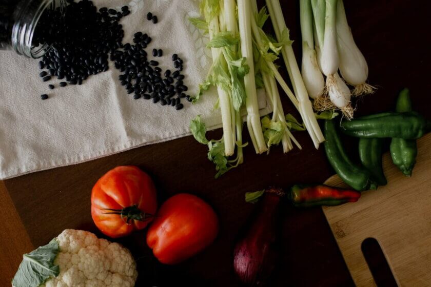 einfache Gerichte / Schwarze Bohnen, Tomaten, Blumenkohl und Frühlingszwiebeln auf einem Holzbrett – unverarbeitete Grundzutaten als Basis klimafreundlicher Ernährung.