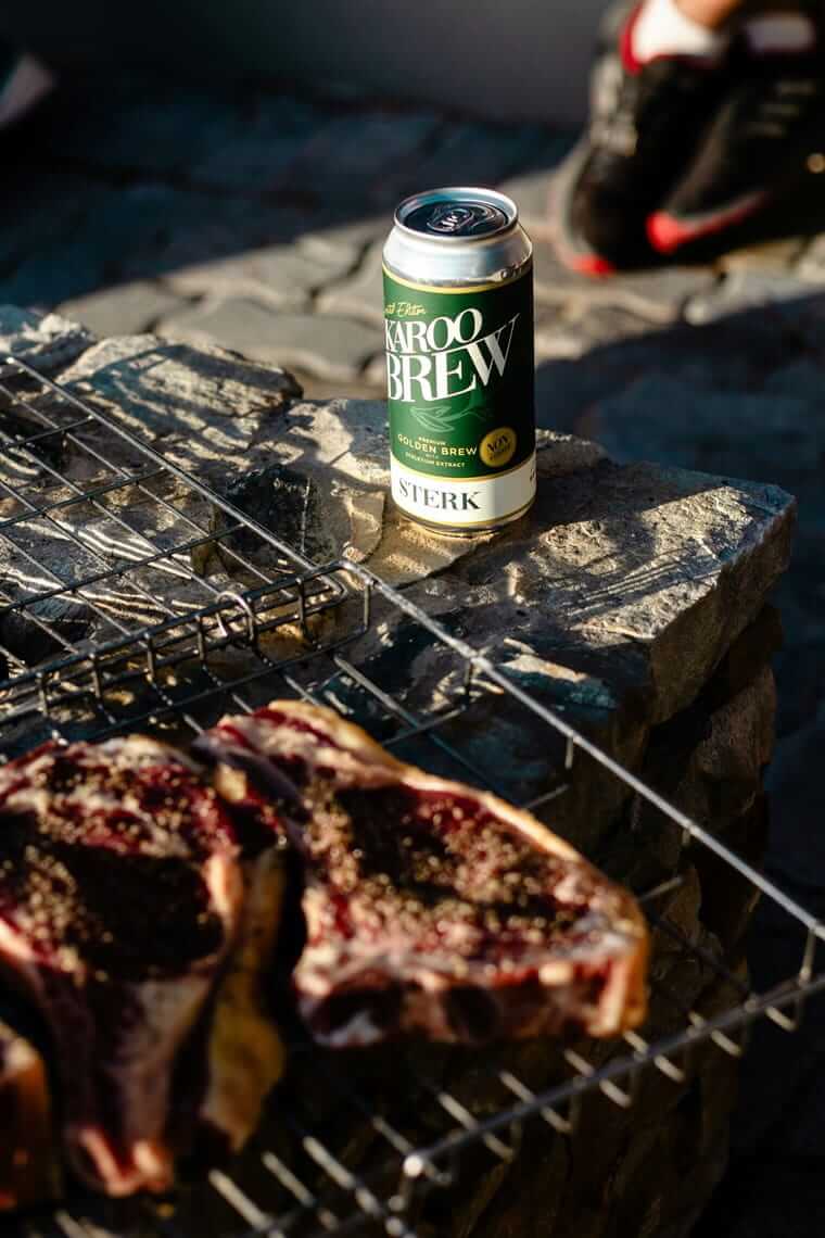 Getränkedose auf einem Steingrill, daneben gegrillte Fleischstücke auf dem Rost