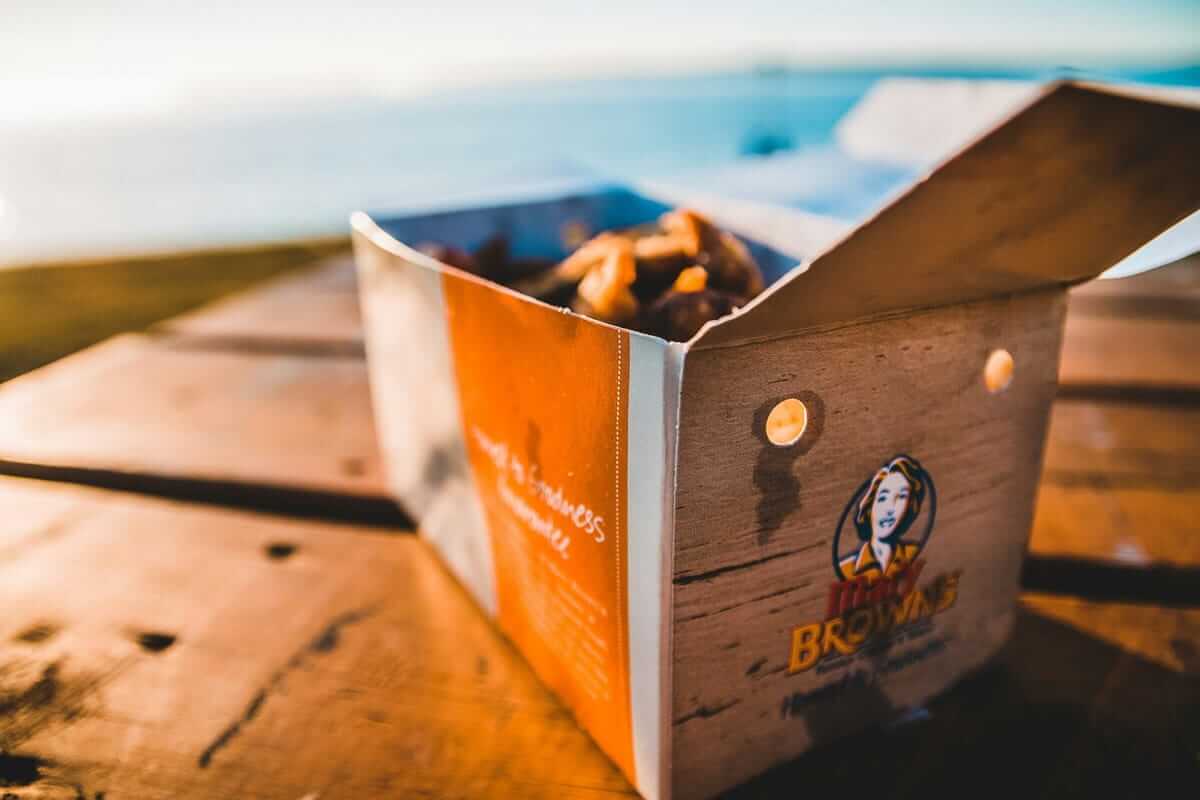 Wenn Überforderung auf den Teller schlägt: Warum bei Erschöpfung zuerst das Essen leidet Erschöpfung / Geöffnete Takeaway-Box mit Essen auf einem Holztisch im Gegenlicht