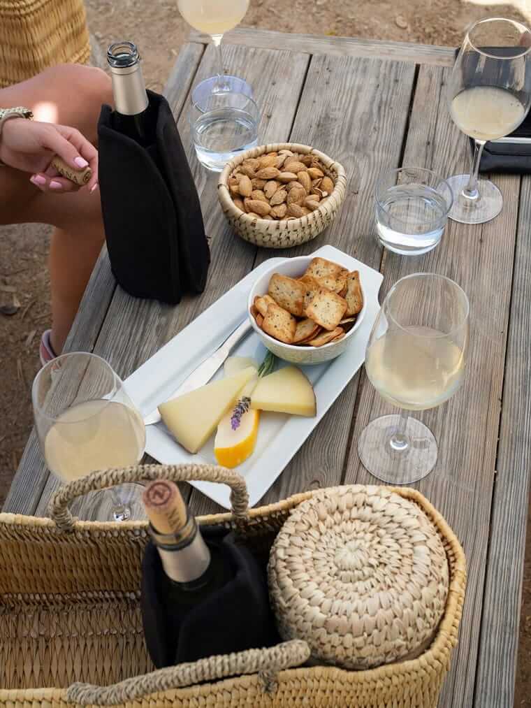 Picknicktisch von oben mit Weißwein im Glas, Käseplatte, Mandeln und Crackern