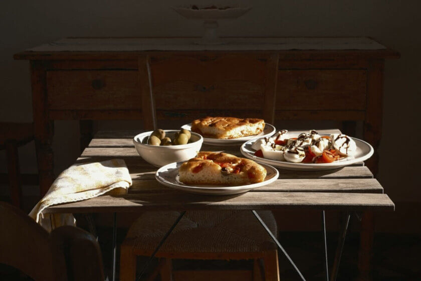 Italienische Küche / Rustikaler Holztisch mit Focaccia, Oliven und Caprese-Salat im Seitenlicht