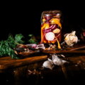 Eingelegtes Gemüse im Glas mit Knoblauch und Kräutern auf einem Holzbrett – Haltbarmachen als Weg gegen Lebensmittelverschwendung im Sommer.