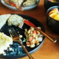 Kleines Frühstück auf schwarzem Teller – Rührei, Toast und eine Schüssel mit frischem Obst, aufgenommen bei warmem Tageslicht