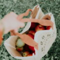 Ressourcenschonung / Hand hält eine Stofftasche mit roten Äpfeln auf einer Wiese
