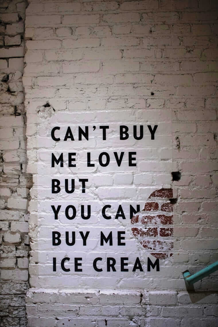 Schriftzug an einer weißen Backsteinwand: ‚Can't buy me love but you can buy me ice cream