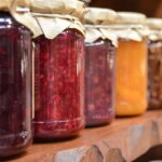 Marmelade verfeinern / Reihe von Gläsern in verschiedenen Farben auf einem Holzregal, Papierverschluss oben.