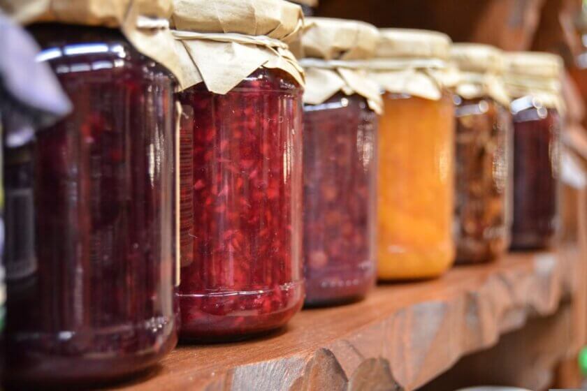 Marmelade verfeinern / Reihe von Gläsern in verschiedenen Farben auf einem Holzregal, Papierverschluss oben.