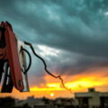 Energy Shots / Rote Metallklemme an einem Kabel vor stürmischem Abendhimmel über Hausdächern