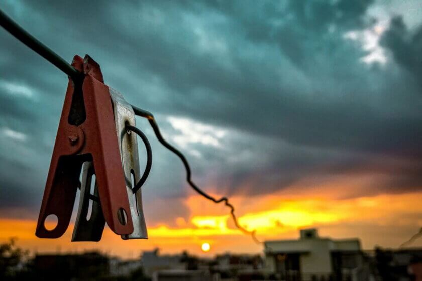 Energy Shots / Rote Metallklemme an einem Kabel vor stürmischem Abendhimmel über Hausdächern